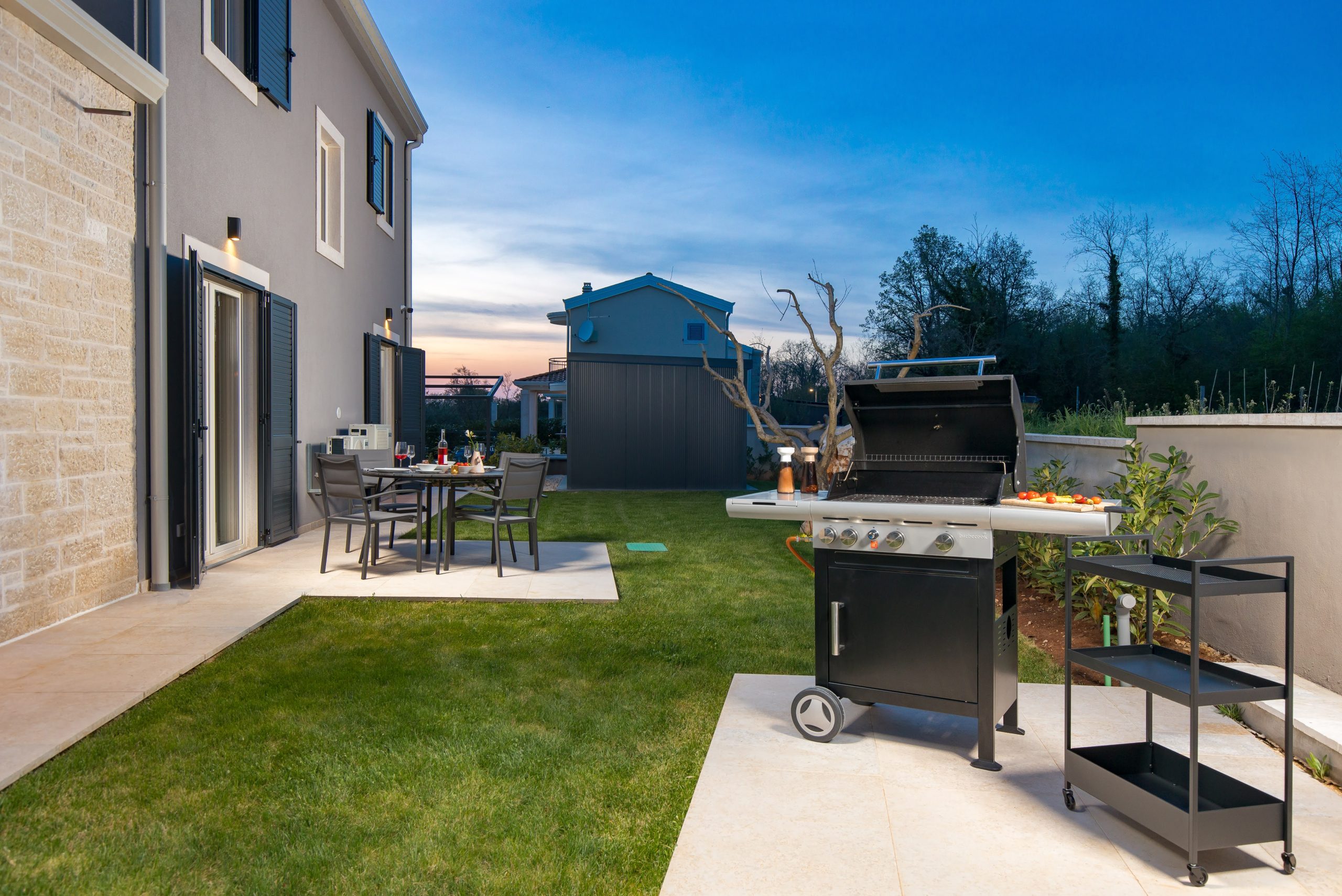 Barbecue grill and dining table in the garden at twilight