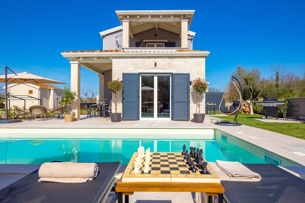 Poolside chess table between sun loungers under the pergola