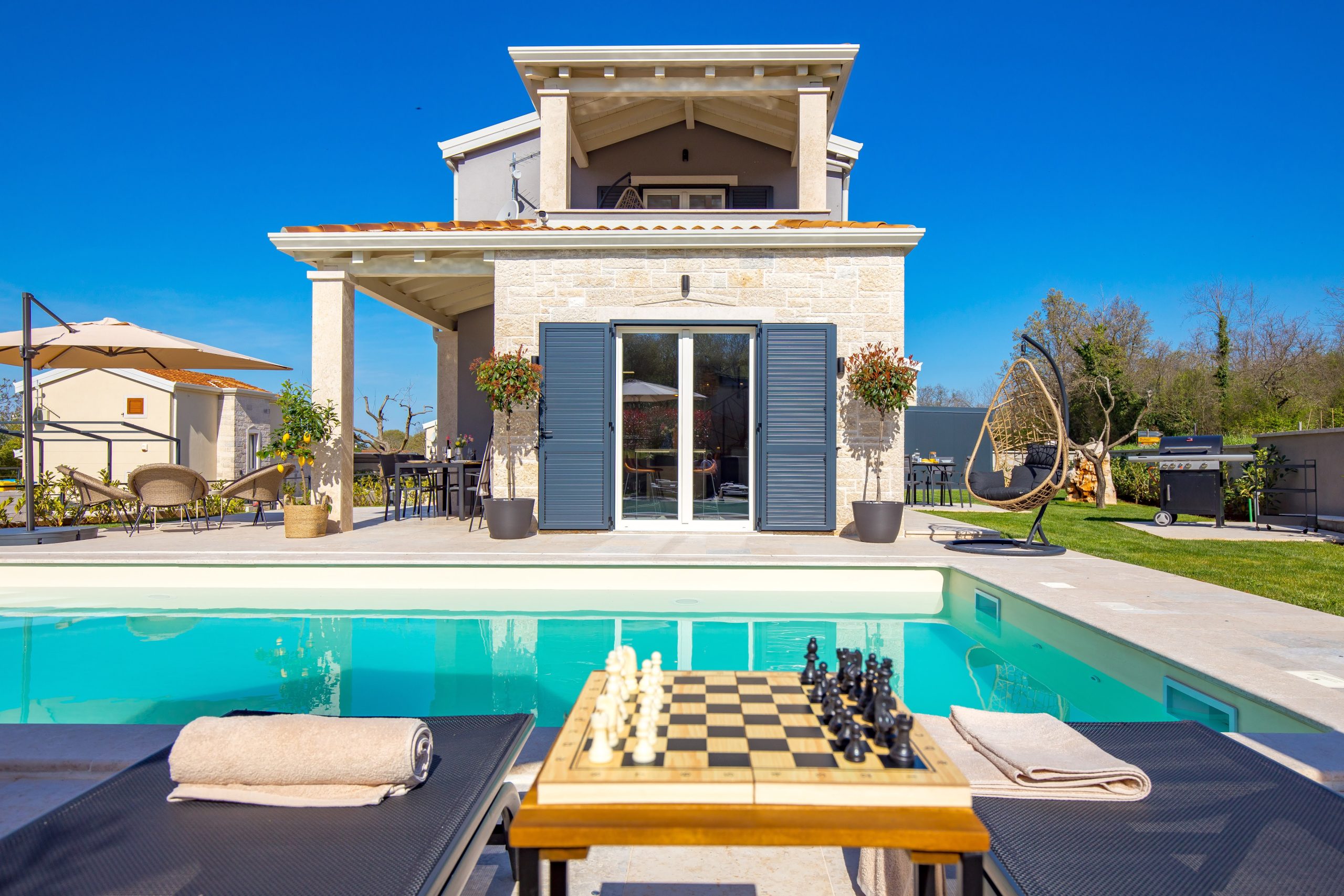 Poolside chess table between sun loungers under the pergola